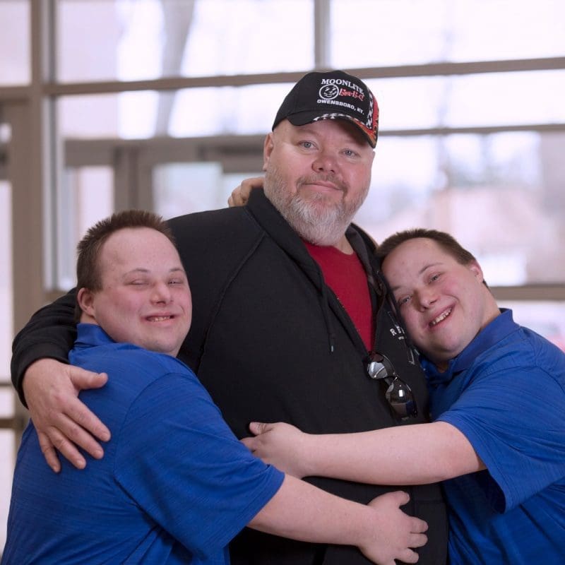 Twin brothers with Down Syndrome hug their father after a happy dentist and doctor appointment.