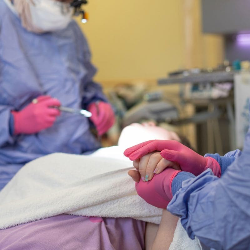 Patient with IDD which could include autism, cerebral palsy, downs syndrome, or other - reclines while one dentist explains a procedure and other dentist holds hand in comfort. Preventative Dental Care is very important for those with IDD.