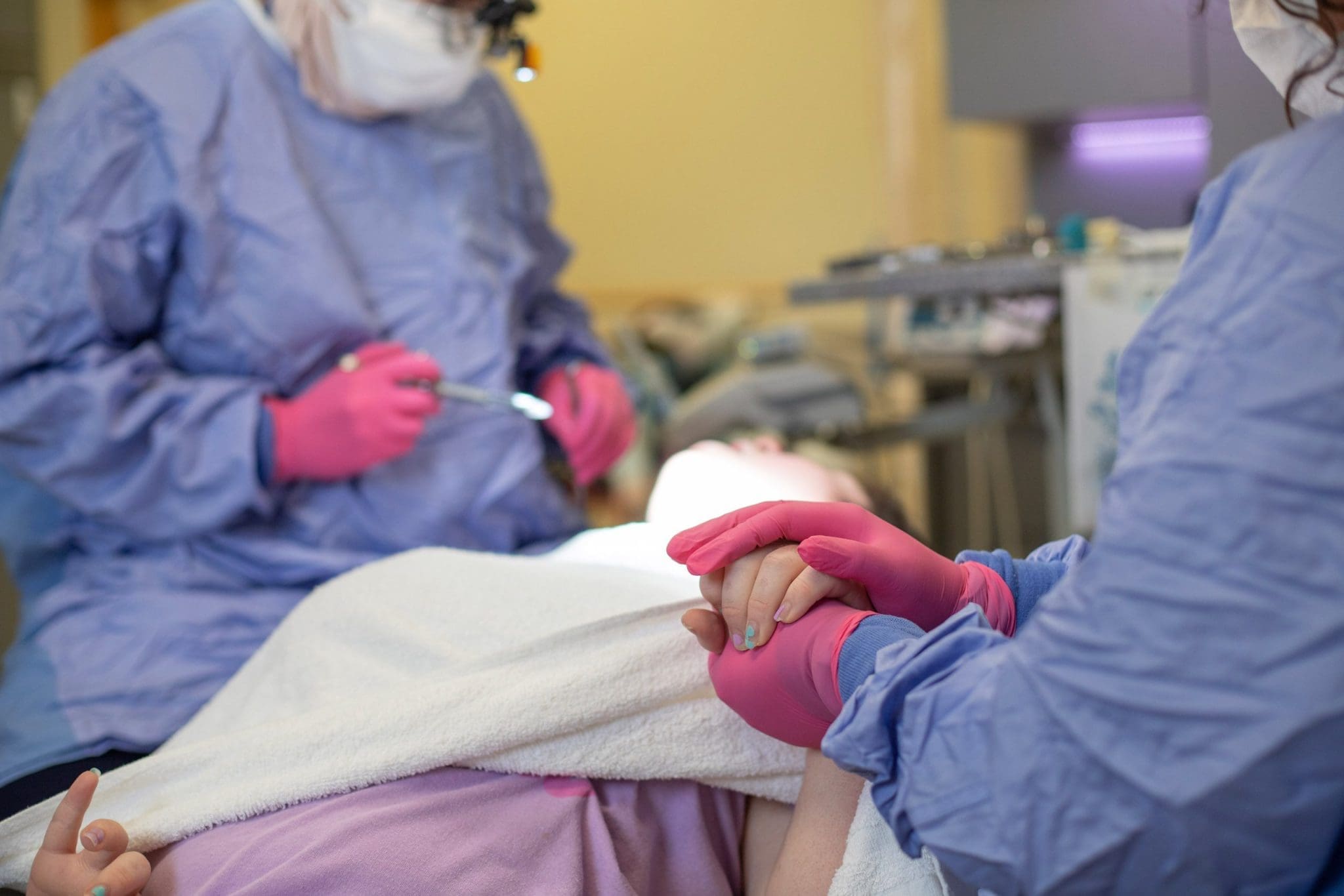 Patient with IDD which could include autism, cerebral palsy, downs syndrome, or other - reclines while one dentist explains a procedure and other dentist holds hand in comfort. Preventative Dental Care is very important for those with IDD.