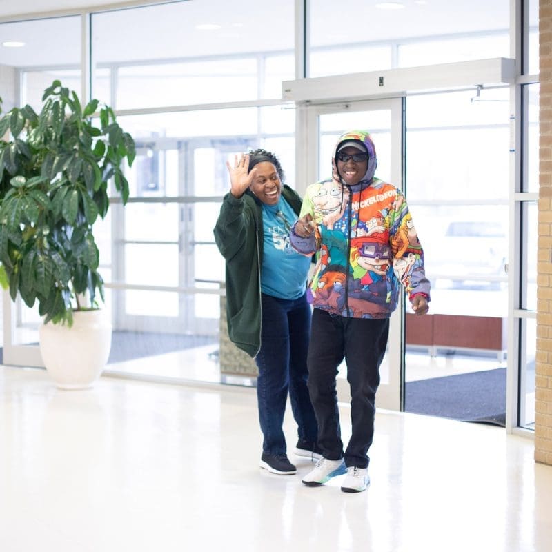 Young man with Autism Spectrum Disorder (ASD) in a brightly colored jacket grins as he walks alongside his smiling mother after a therapy appointment, feeling accomplished and supported.