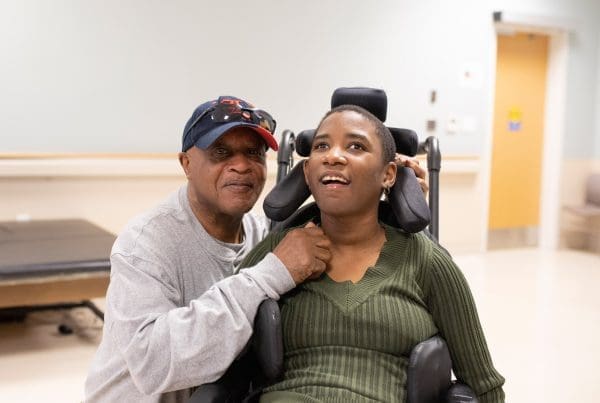 Father smiling next to his daughter who is in a wheel chair.