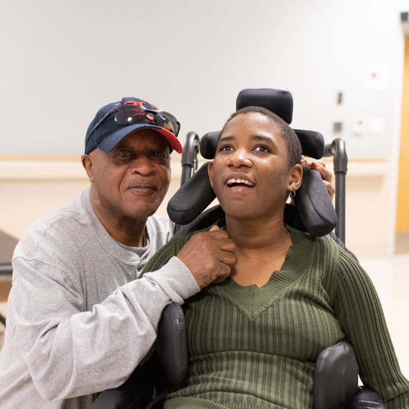 Father smiling next to his daughter who is in a wheel chair.