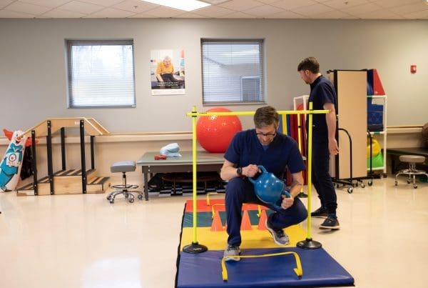 Two therapists set up a dynamic obstacle course to support mobility, coordination, and balance training for patients with intellectual and developmental disabilities (IDD) in a physical rehabilitation session.