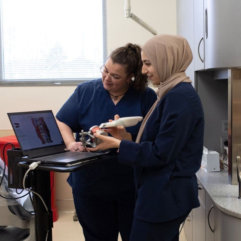 A skilled dentist wearing a hijab teaches a student dentist proper examination techniques during a hands-on training session in a specialized dental clinic for individuals with intellectual and developmental disabilities (IDD)
